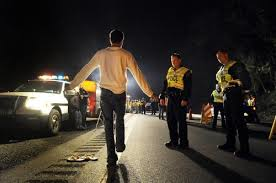 Law Office of Kevin Bessant A person performs a sobriety test on a road at night, observed by three police officers and a police car with flashing lights, while the nearby Law Office of Kevin Bessant oversees the procedure.