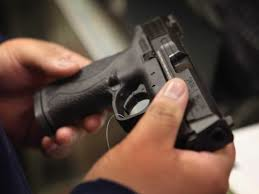 Close-up of a person holding a black Detroit Gun handgun with both hands, focusing on the intricate details of the firearm.