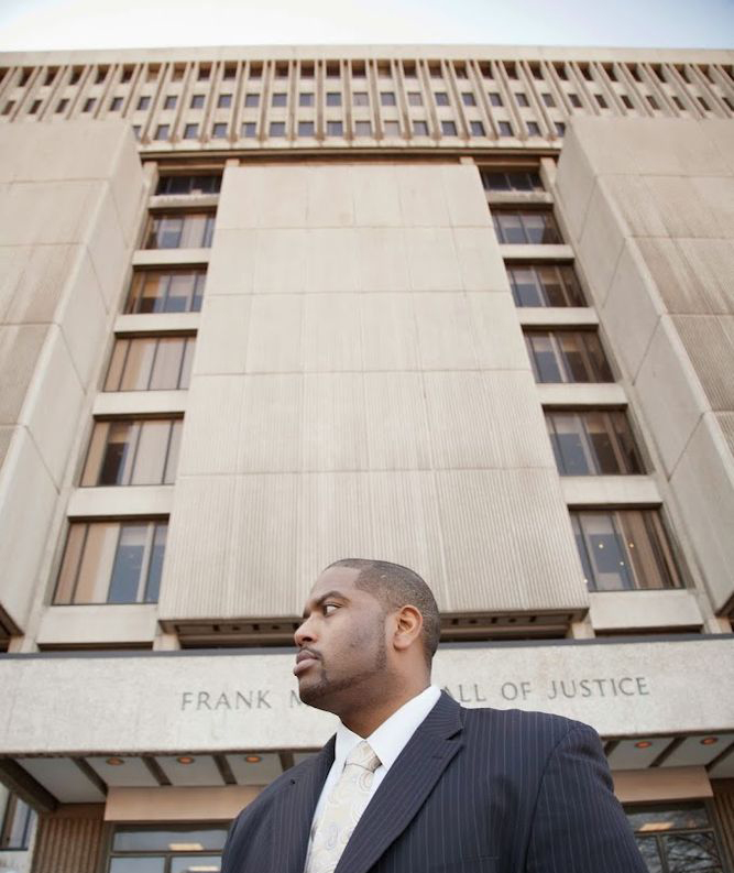 Detroit Criminal Defense Attorney Kevin Bessant A man in a suit stands in front of a large building labeled "FRANK M...", embodying the professionalism and dedication of a top-tier Detroit Criminal Defense Attorney.
